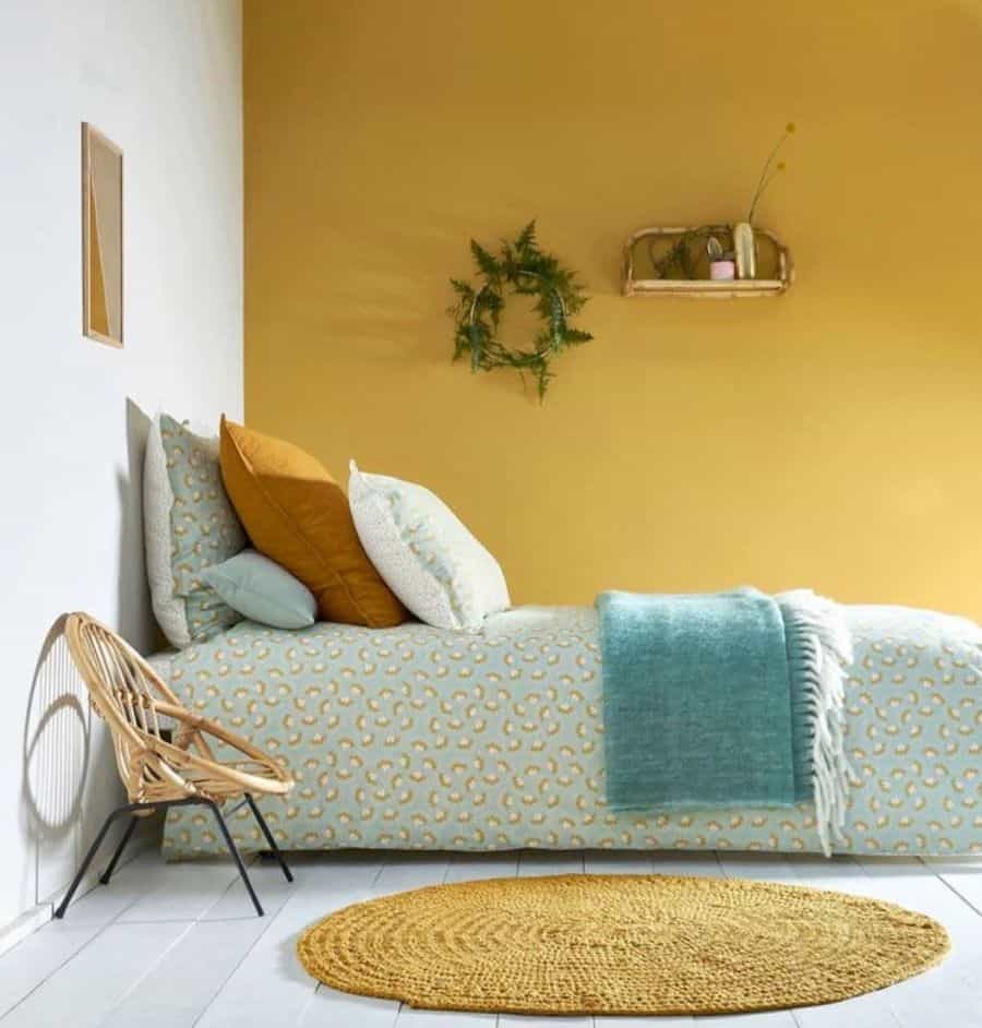 Cozy bedroom with bright yellow and white decor, patterned bedding, wicker chair, and a circular rug on white floorboards