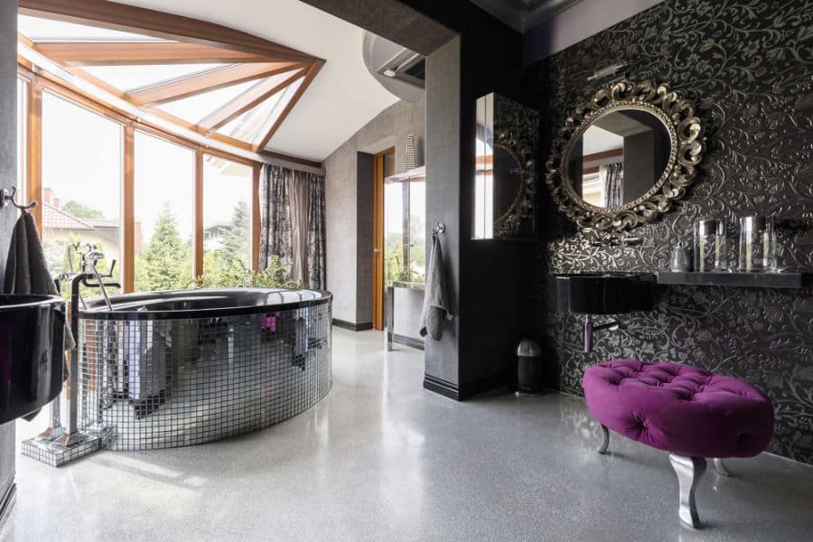 Bathroom with silver-tiled bathtub, ornate mirror, textured wallpaper, and purple seating.