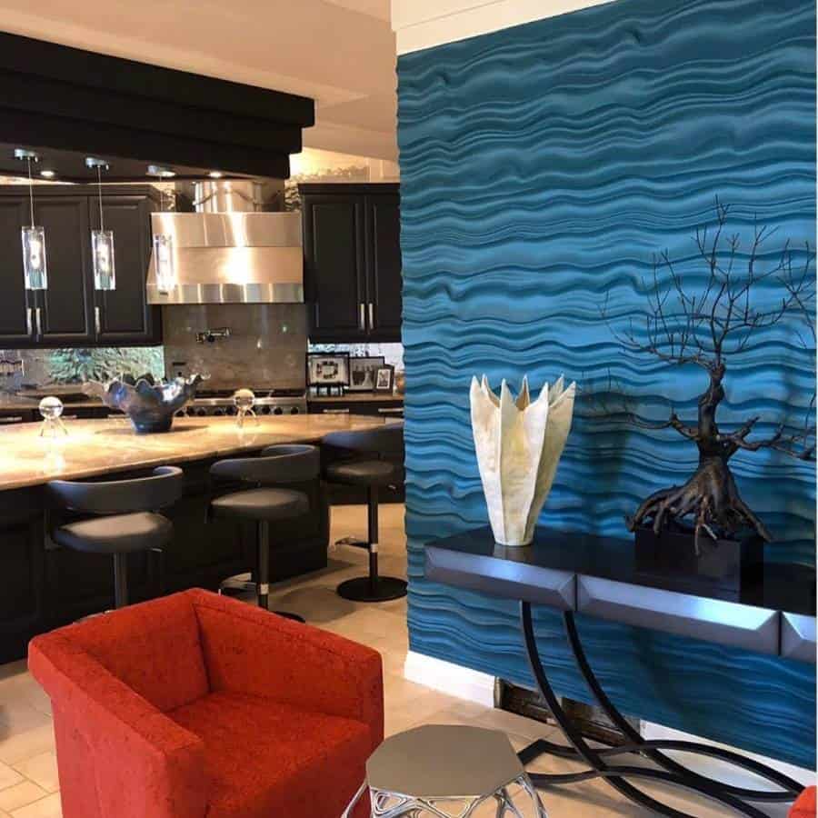 Modern kitchen with a blue accent wall, black cabinets, and red chair; decorative items on black console table