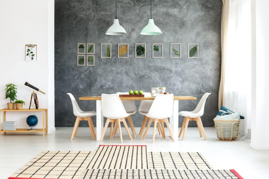 Modern dining room with a wooden table, six white chairs, an accent chalkboard wall, and framed plant art