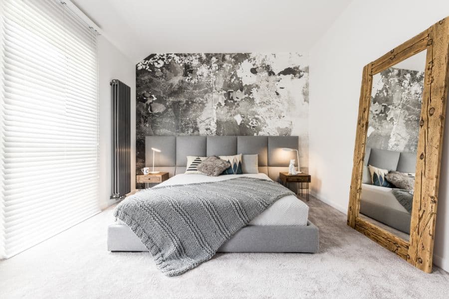 Modern bedroom with accent wall, large mirror, and a cozy bed with layered pillows and blankets