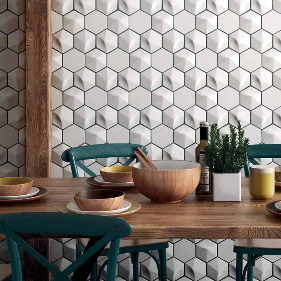 Dining table with wooden bowls, green chairs, and an accent wall of geometric white tiles
