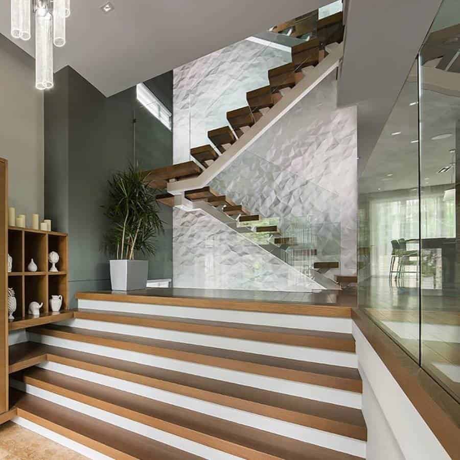 Modern interior with an accent wall, wooden staircase, glass railings, a plant, and a bookshelf on the side