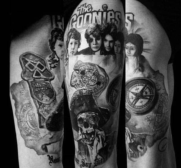 Black and gray tattoo sleeve inspired by *The Goonies*, featuring the main characters, treasure maps, a pirate skull, a compass, and the movie title.