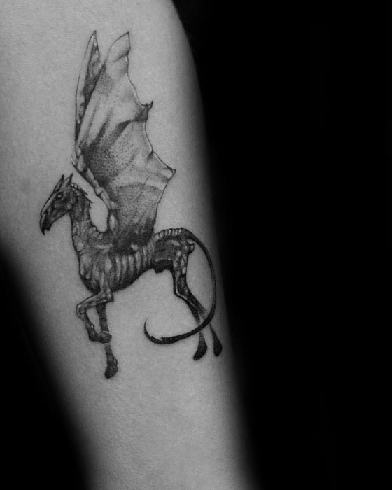 Small Thestral tattoo with fine linework and delicate shading, capturing its skeletal form and wings in a minimal style on the arm.