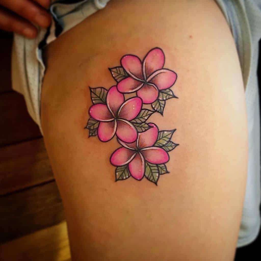 A vibrant tattoo of three pink plumeria flowers with lush green leaves graces a person's arm