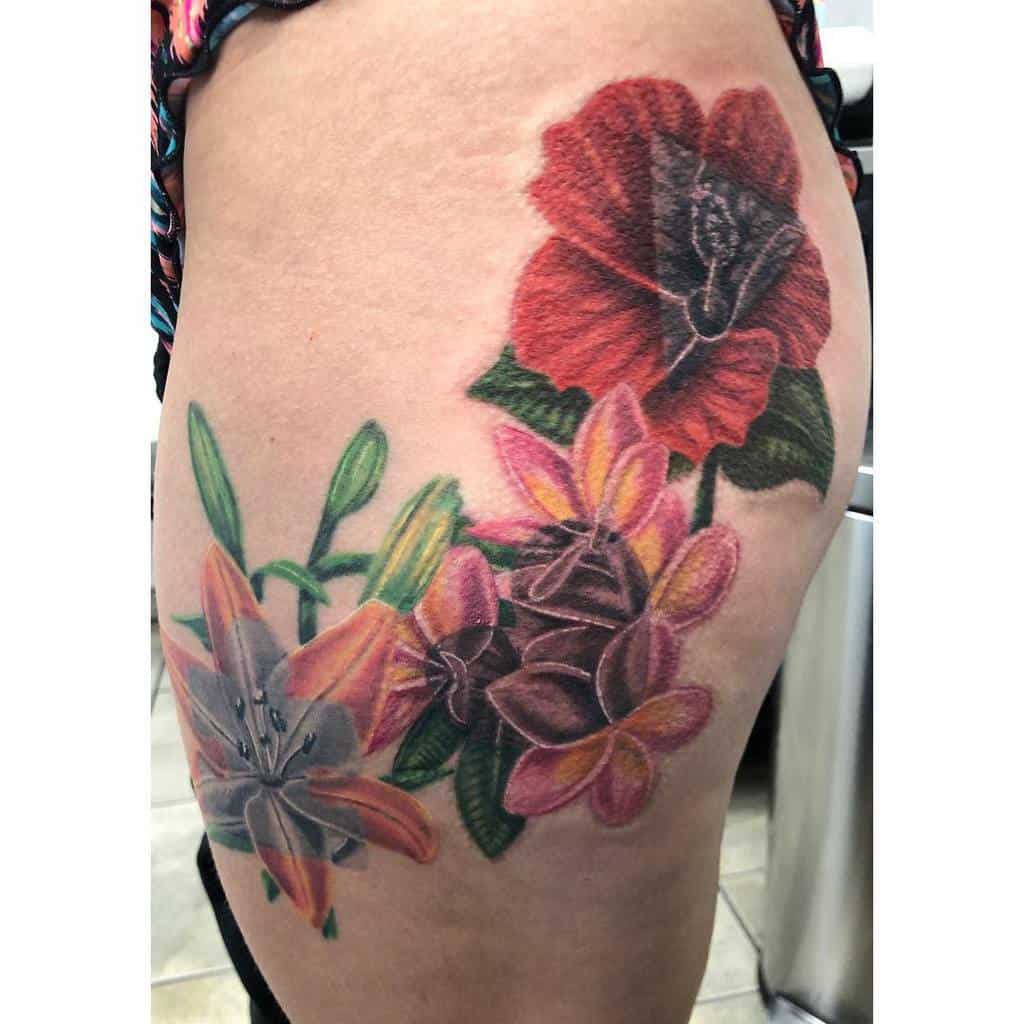 A vibrant floral tattoo featuring lilies, roses, and plumeria adorns a person's upper thigh