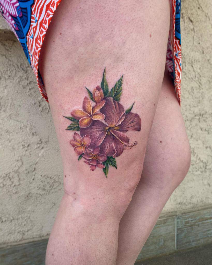 Colorful floral tattoo of hibiscus and plumeria on a thigh