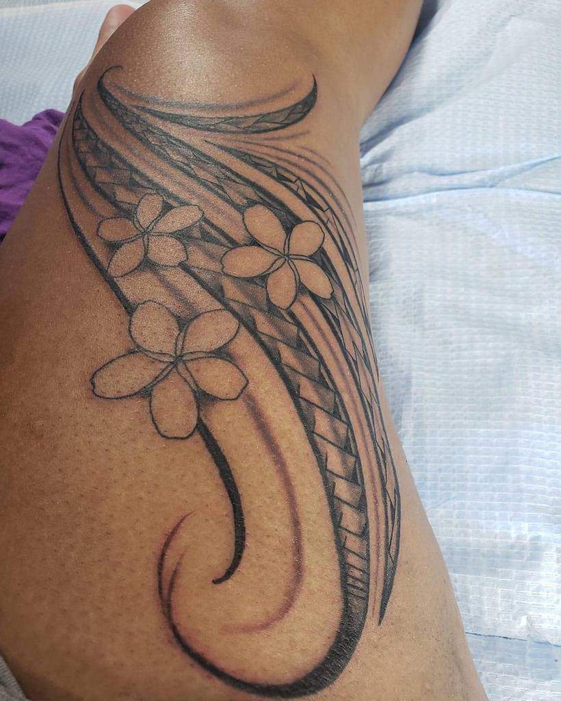 A bold Polynesian-inspired thigh tattoo featuring Plumeria flowers intertwined with flowing tribal patterns, showcasing a harmonious blend of tradition and natural beauty