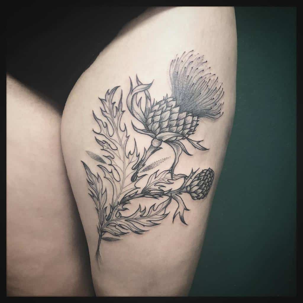 A thigh tattoo of a meticulously detailed black and gray thistle flower