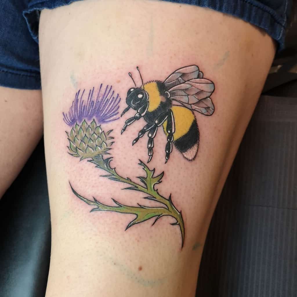 Tattoo of a bee gently hovering near a vibrant thistle flower on a thigh