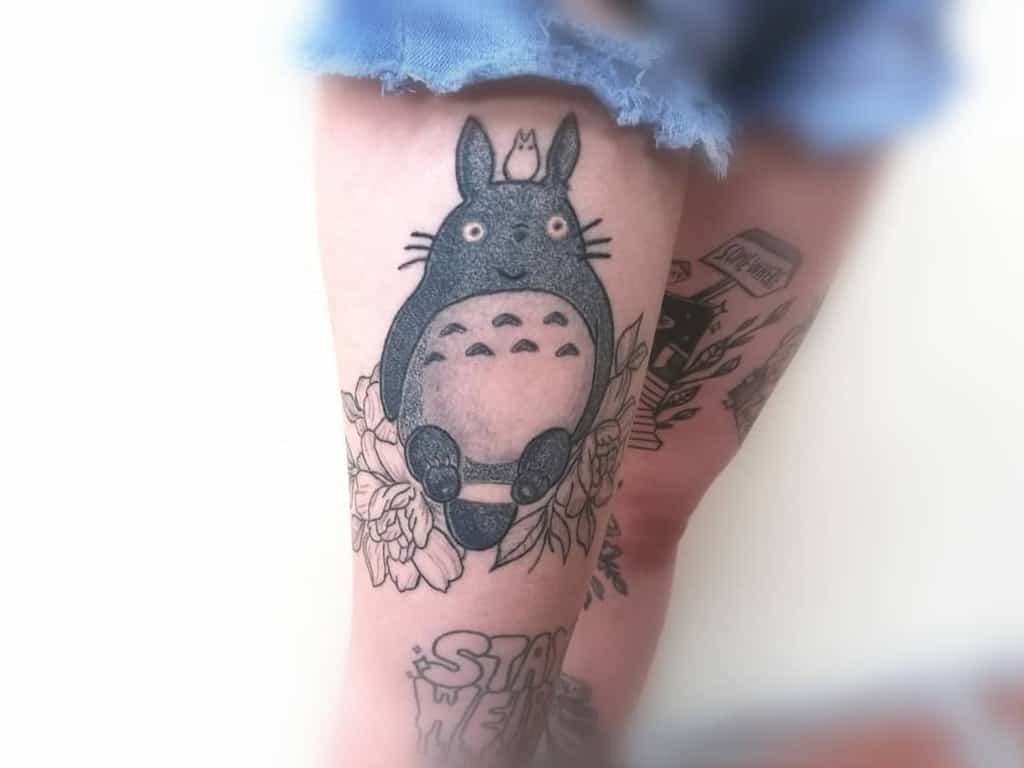 Black and grey Totoro thigh tattoo with intricate floral details, giving it a soft and elegant touch