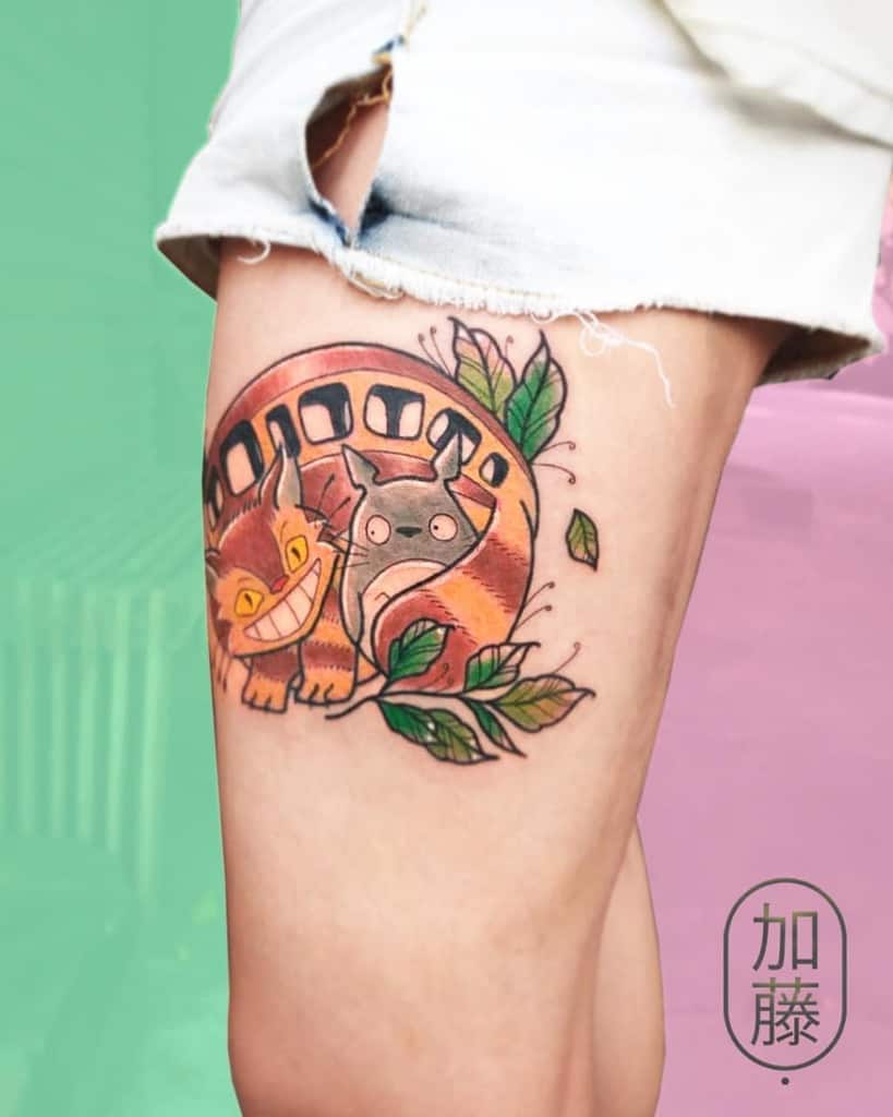 Colorful catbus tattoo with leafy details on a person's thigh