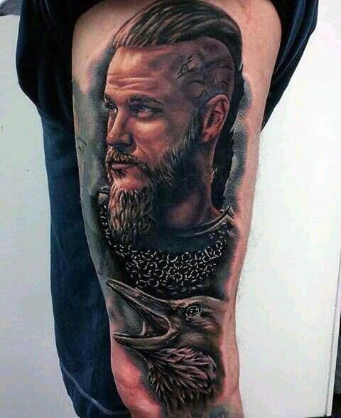 Vivid tattoo of Ragnar Lothbrok in chainmail, with a raven below and intricate details.