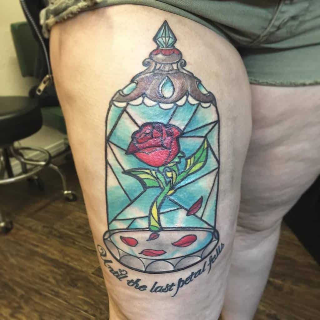 Tattoo of a rose in a glass case with text "until the last petal falls" on a person's thigh