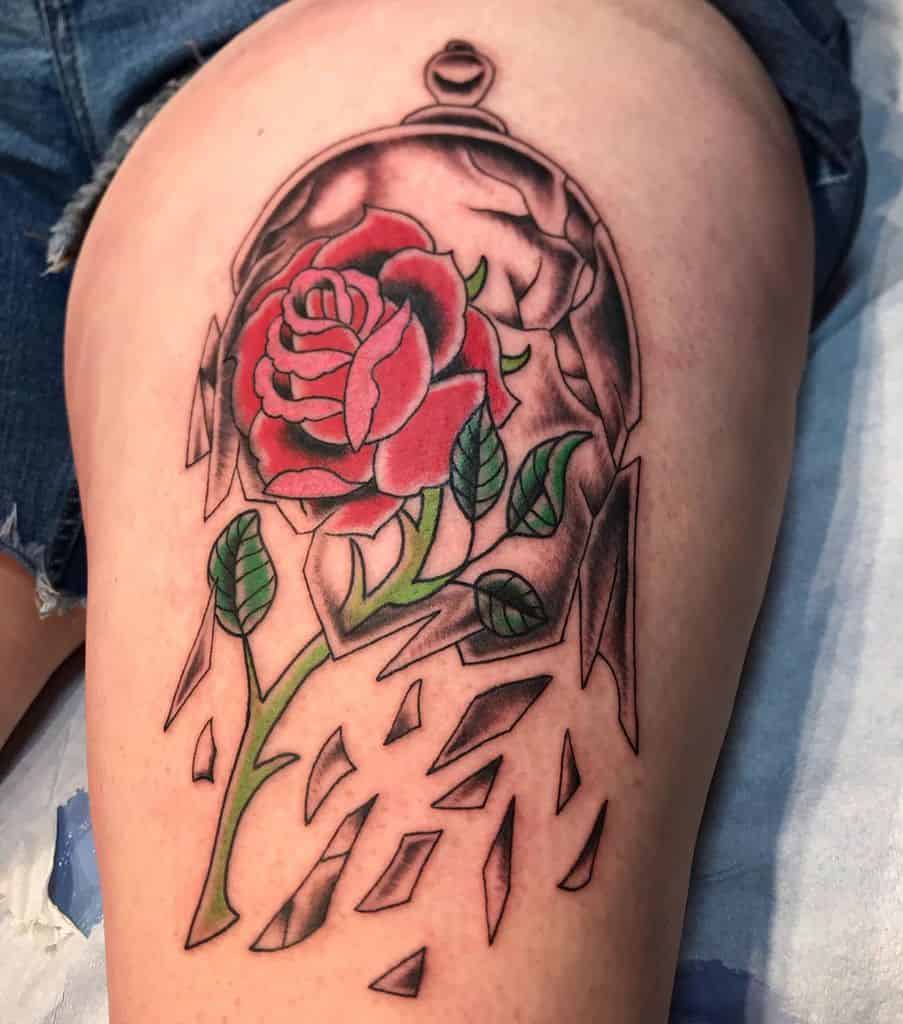 Tattoo of a rose under a cracked glass dome with scattered shards on a thigh