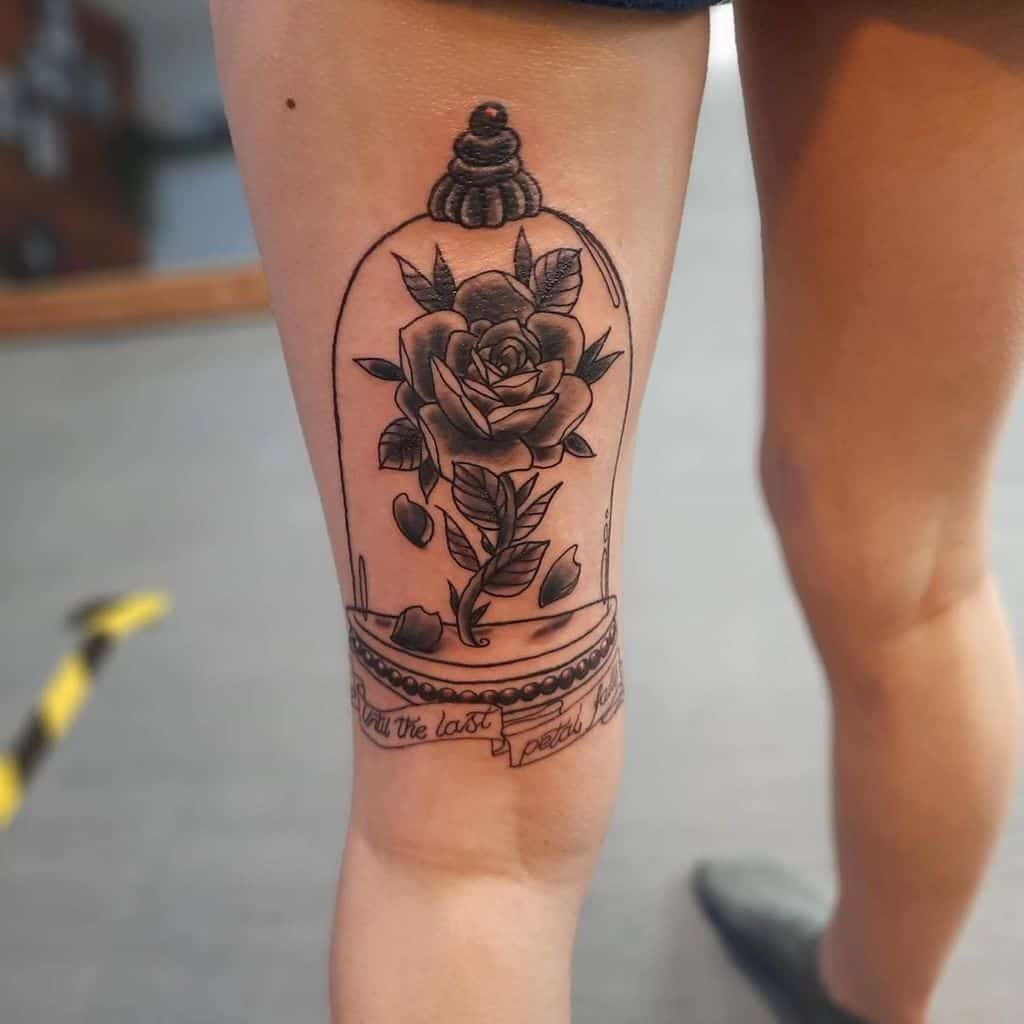 A black and grey Beauty and the Beast rose tattoo inside a glass dome, with intricate details and the phrase "Till the last petal falls" beneath it