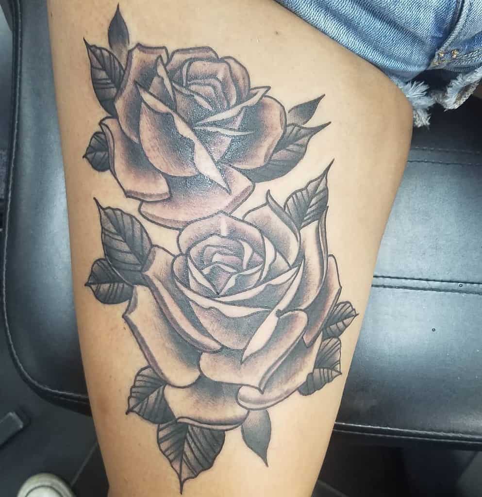 Tattoo of two shaded roses with leaves on a person's thigh