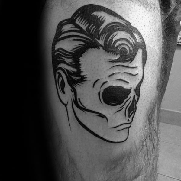 Black and white tattoo of a skull with a slicked-back hairstyle, showcasing clean lines and bold contrast, placed on the thigh.