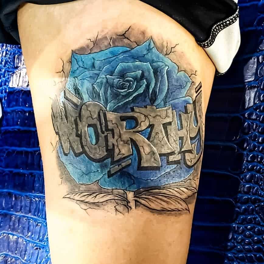 Thigh tattoo of a blue rose with "WORTHY" written in graffiti style over it