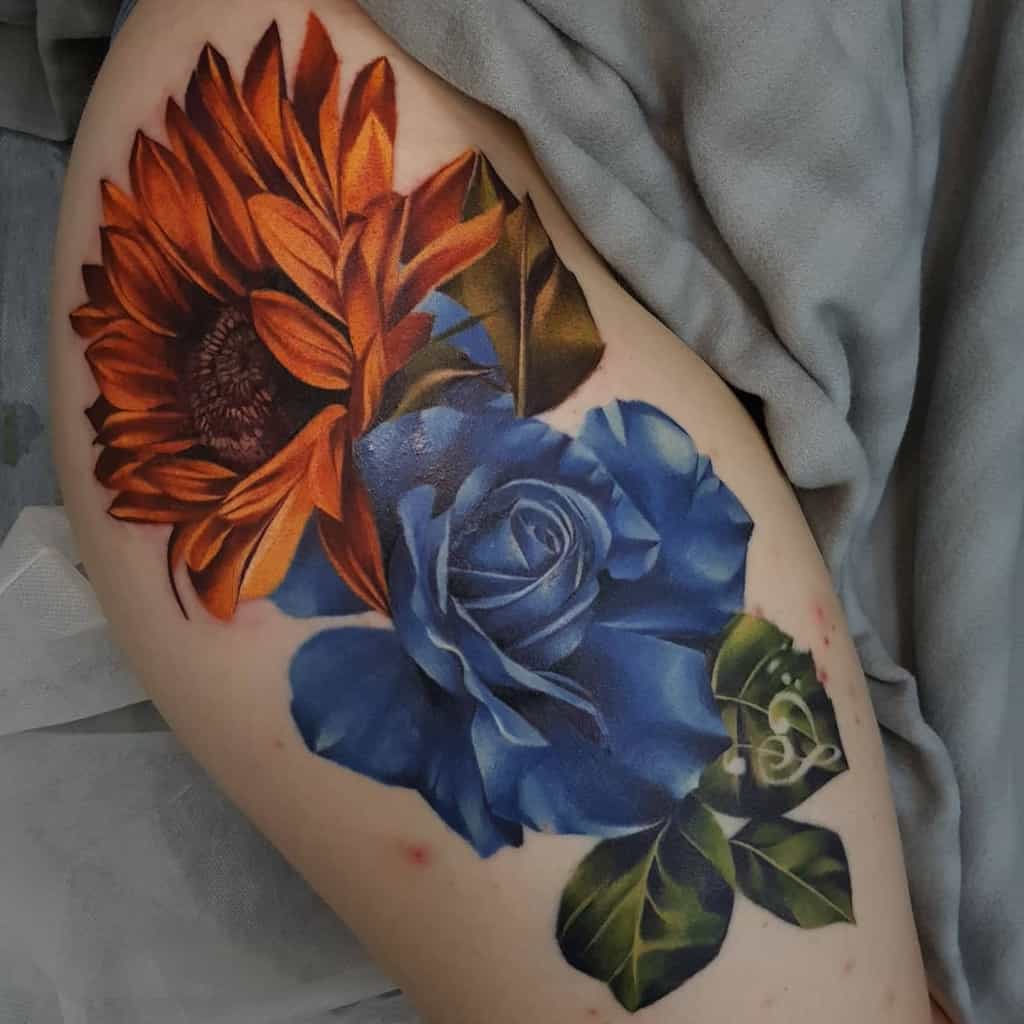 Tattoo of an orange sunflower and a blue rose with green leaves on a thigh