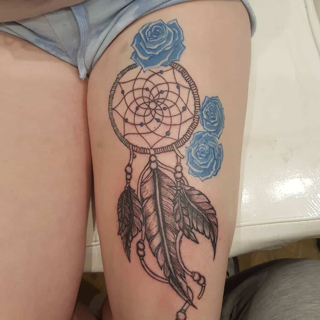 Thigh tattoo of a dreamcatcher with feathers and three blue roses