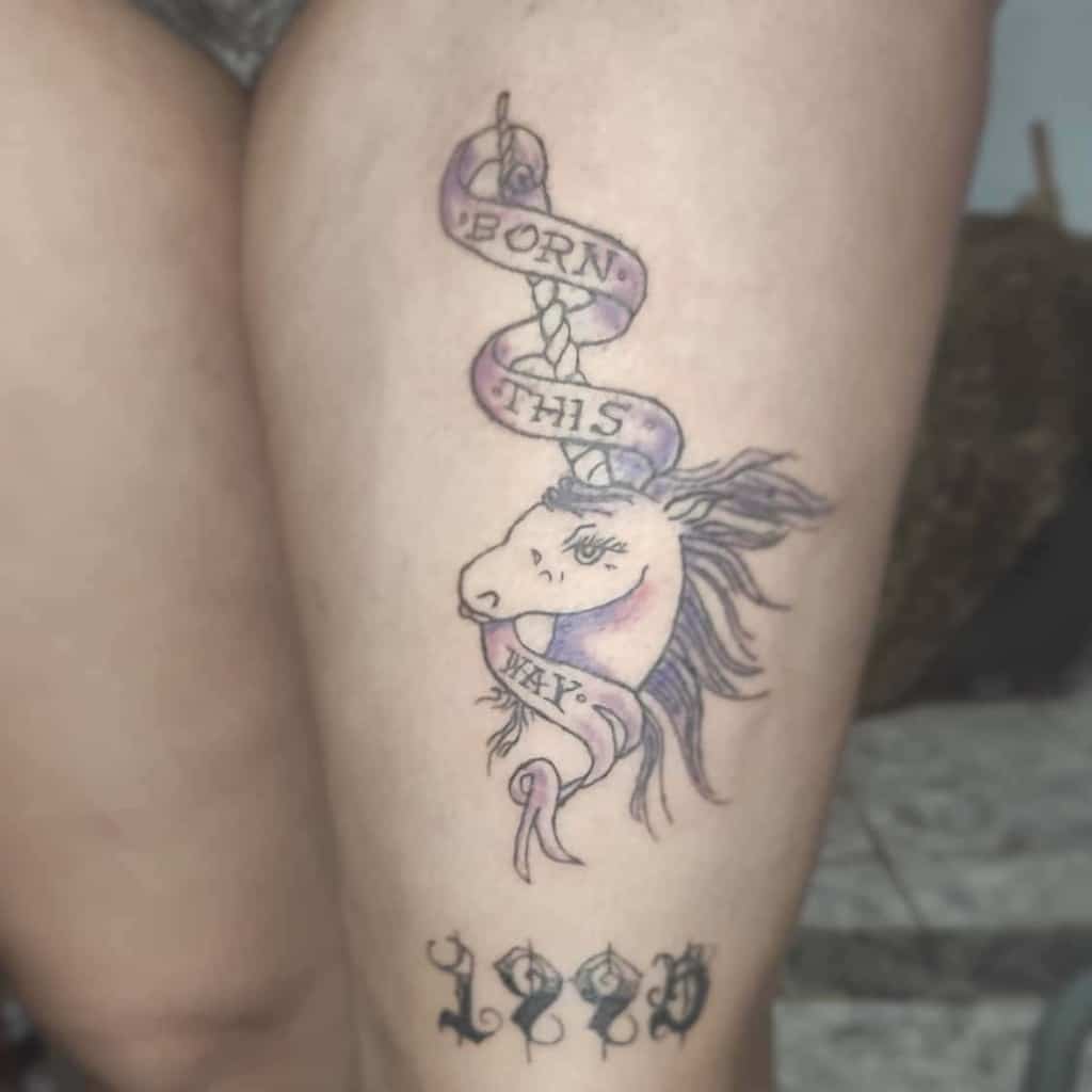 A unicorn tattoo with a "Born This Way" ribbon on a leg, and "1990" inked below