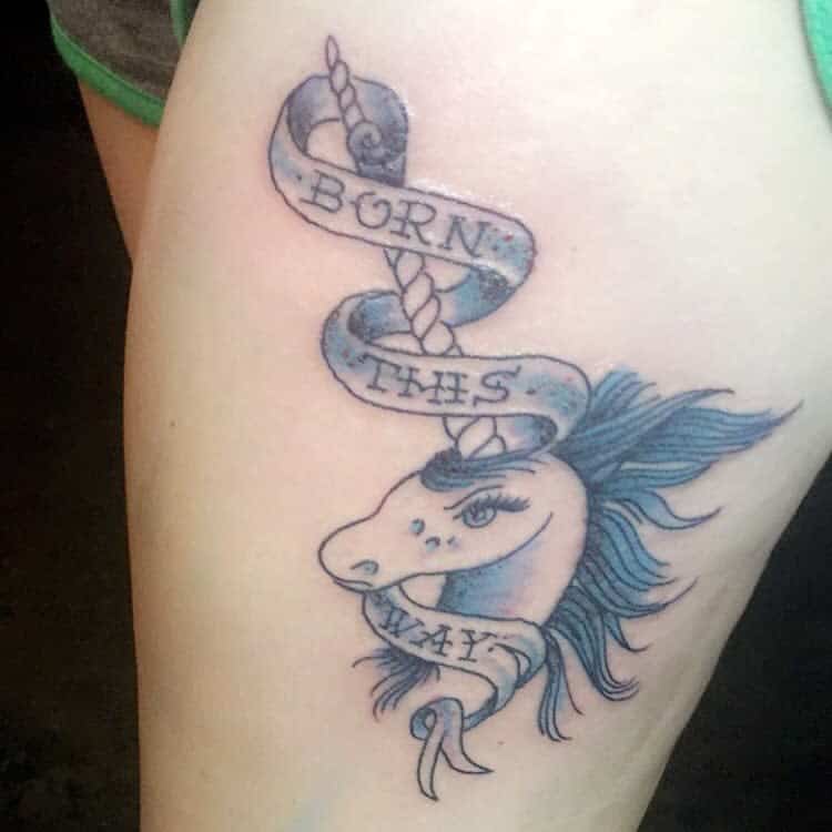 Tattoo of a blue unicorn with a banner reading "Born This Way" wrapped around its horn