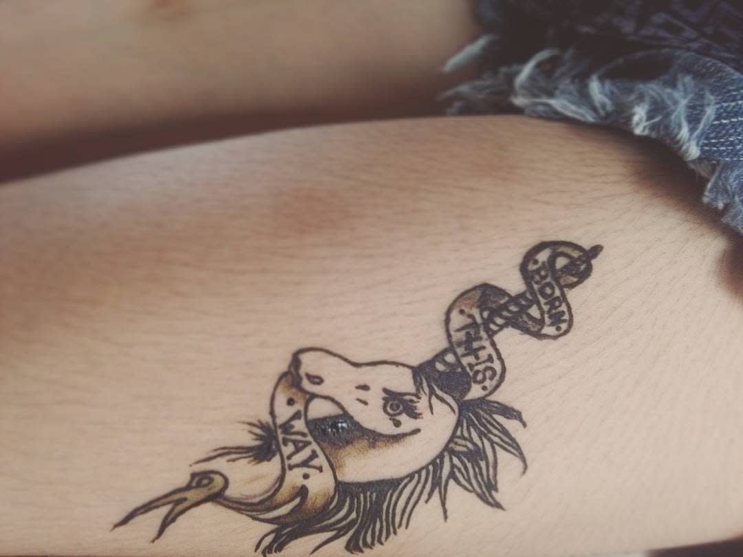 Tattoo of an unicorn with a ribbon that says "Born This Way" on a person's skin