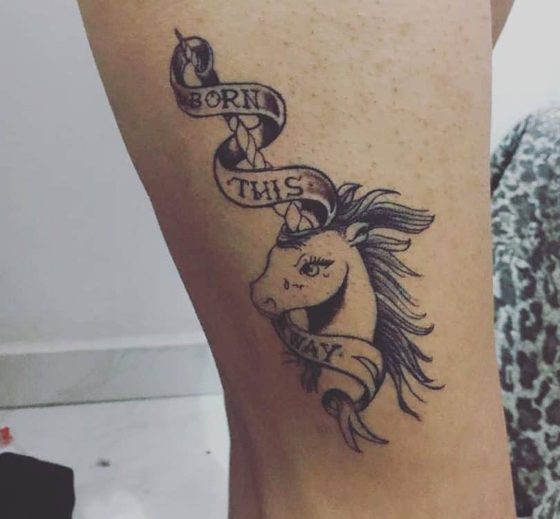 Unicorn tattoo with a ribbon saying "Born This Way" on a thigh