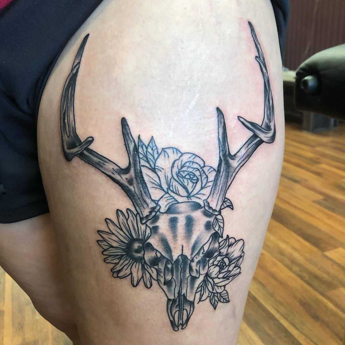 Deer skull tattoo featuring elegant antlers and delicate flowers on a thigh