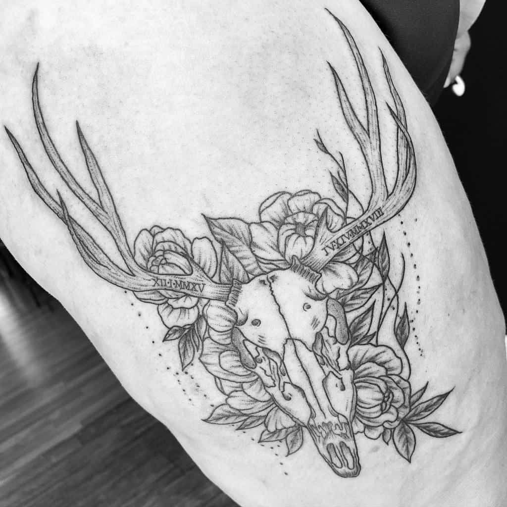 A tattoo featuring a deer skull with antlers, beautifully surrounded by intricate flowers and significant dates