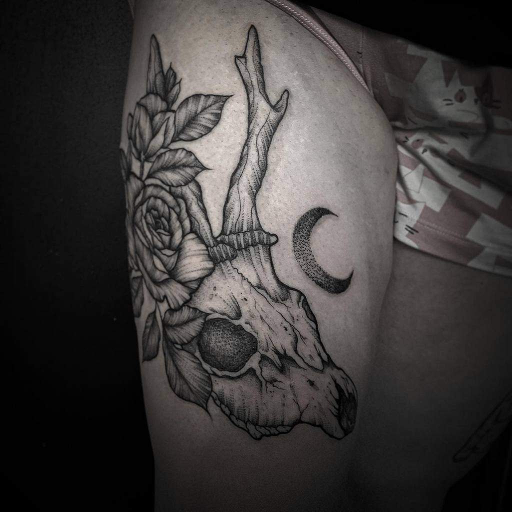 Tattoo on thigh featuring a beautifully detailed deer skull adorned with vibrant flowers and framed by a delicate crescent moon