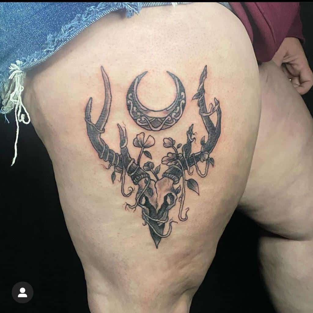 Tattoo of a deer skull with antlers and a crescent moon on the upper thigh of a person, blending nature's mystique with celestial allure
