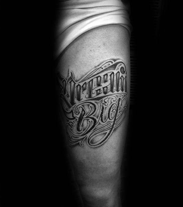 Thigh tattoo featuring the phrase “Dream Big” in dramatic blackletter script with heavy shading and intricate detailing.