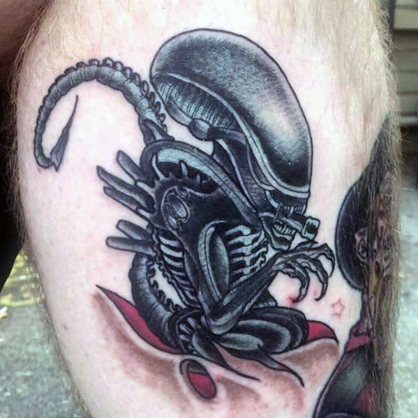 Cartoon-style Xenomorph tattoo with bold outlines and shading, showing the alien crouched with a curled tail and red splash background.