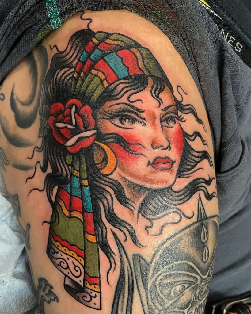 A colorful tattoo of a gypsy woman with a striped headscarf, red rose, and bold outlines, on the upper thigh