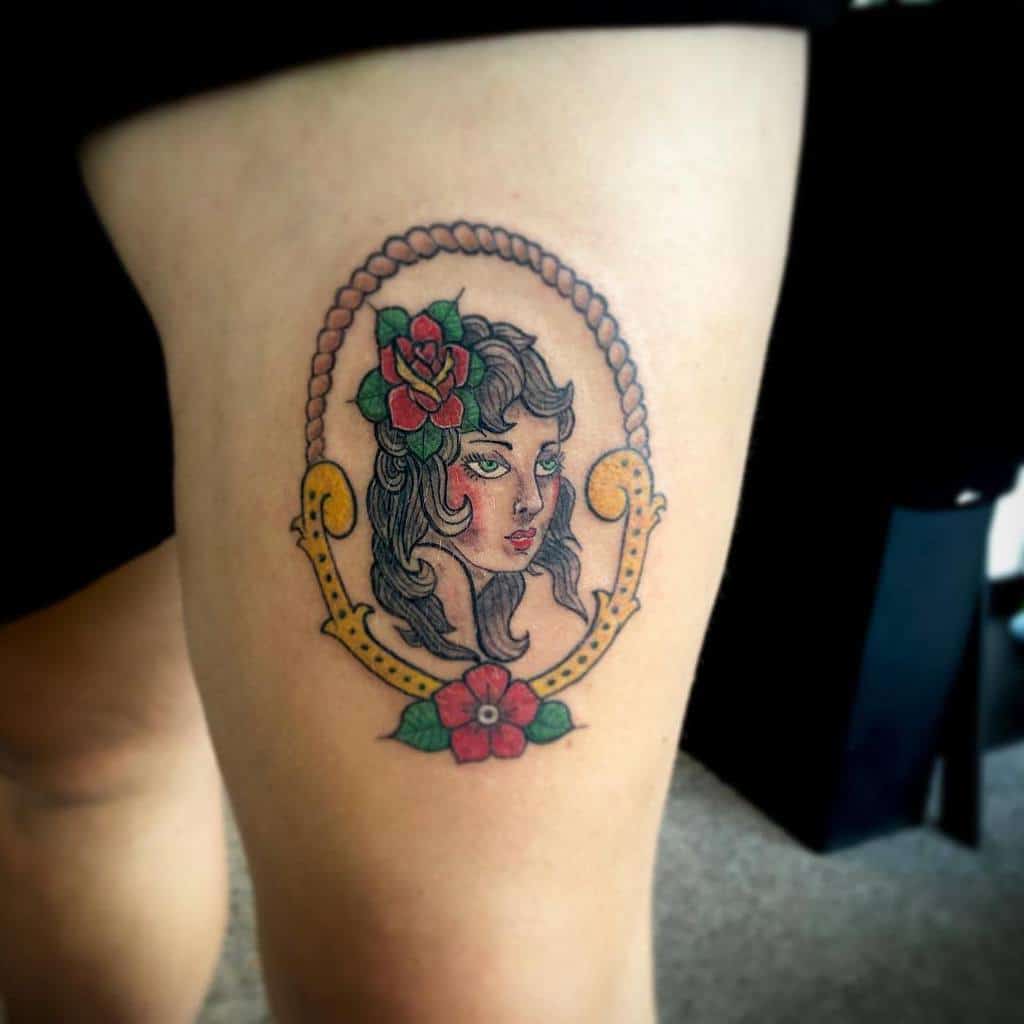 A vintage-style tattoo of a gypsy woman's face adorned with flowers elegantly graces a leg
