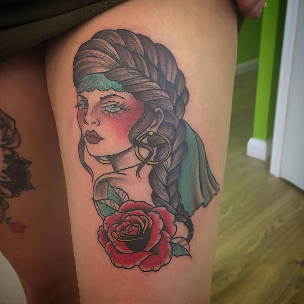 Tattoo of a gypsy woman with braids and a rose on a person's thigh