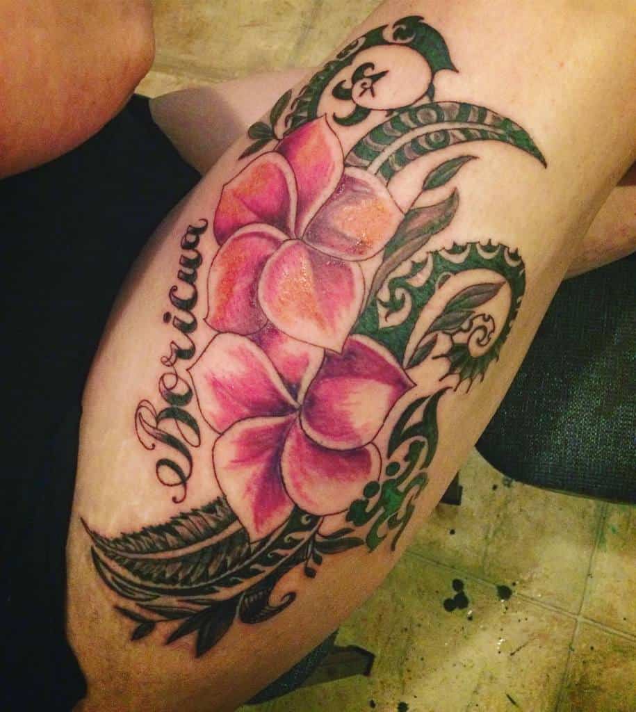 Thigh tattoo featuring bold pink plumeria flowers, green leaves, and intricate black tribal patterns, with the word 'Boricua' scripted