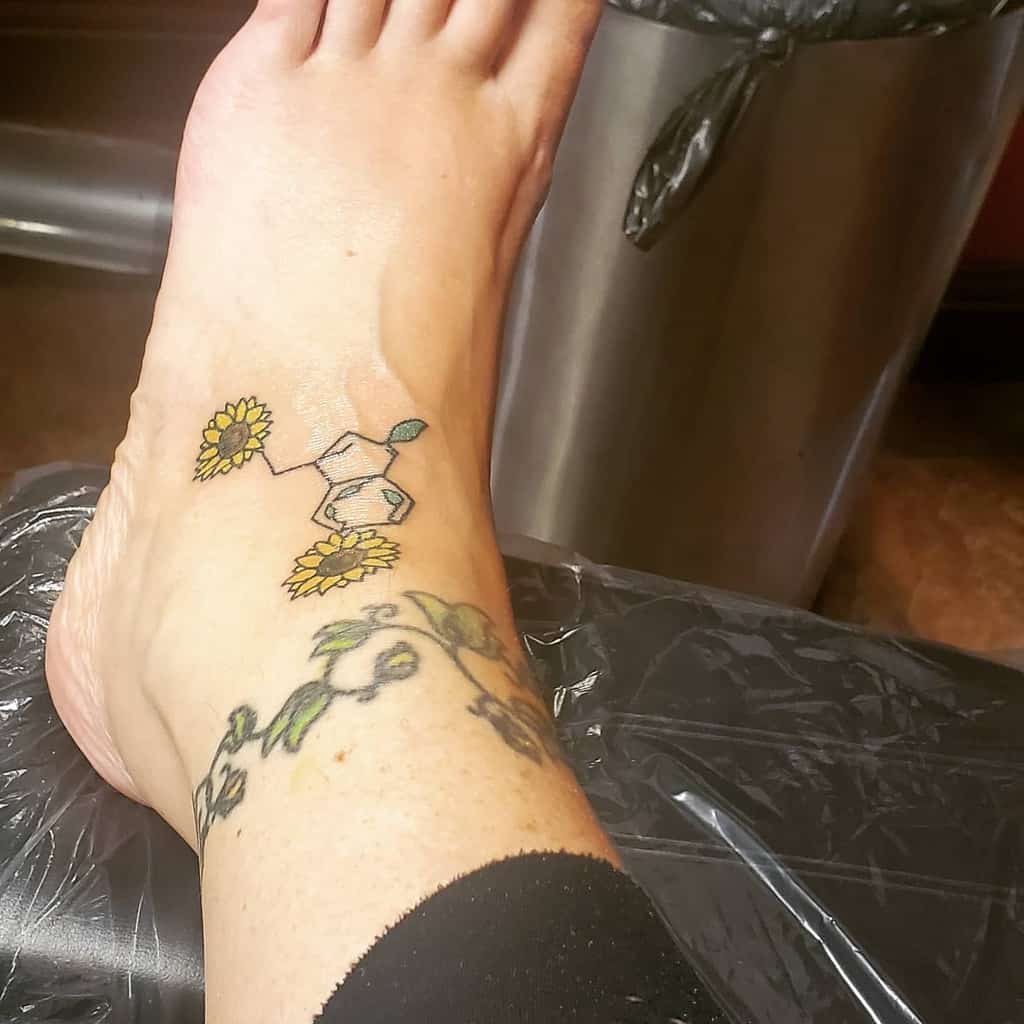 A foot adorned with a tattoo of a serotonin molecule intertwined with vibrant sunflowers