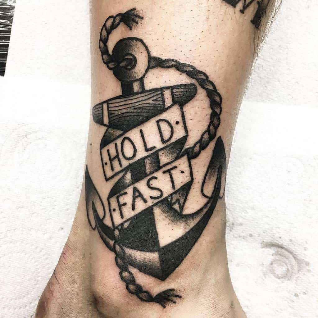 Tattoo of an anchor with a rope and the words "Hold Fast" on a lower leg