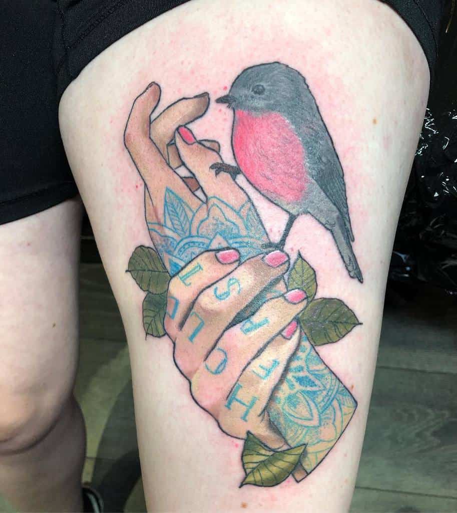Intricate thigh tattoo of 'Hold Fast' on hands holding a vibrant robin perched among green leaves