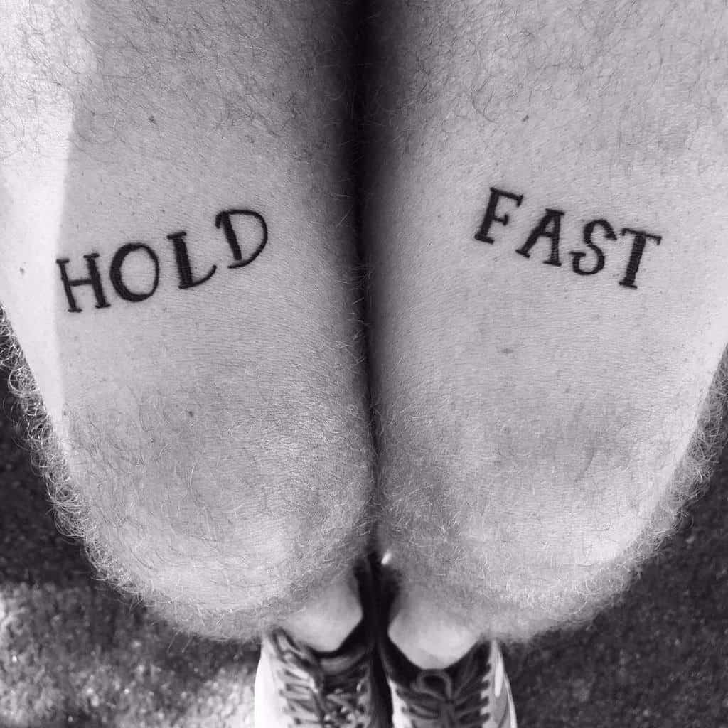 Black and white image of legs with "HOLD FAST" tattooed on each thigh