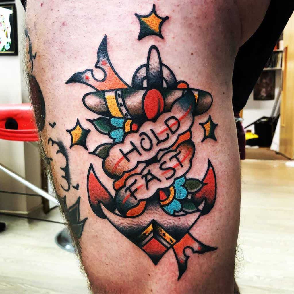 Tattoo of an anchor with "Hold Fast" text, colorful flowers, and orange stars