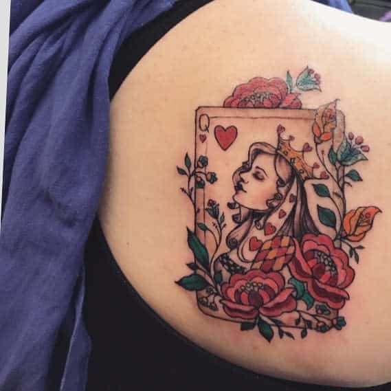 Queen of hearts tattoo with floral and butterfly details on the shoulder