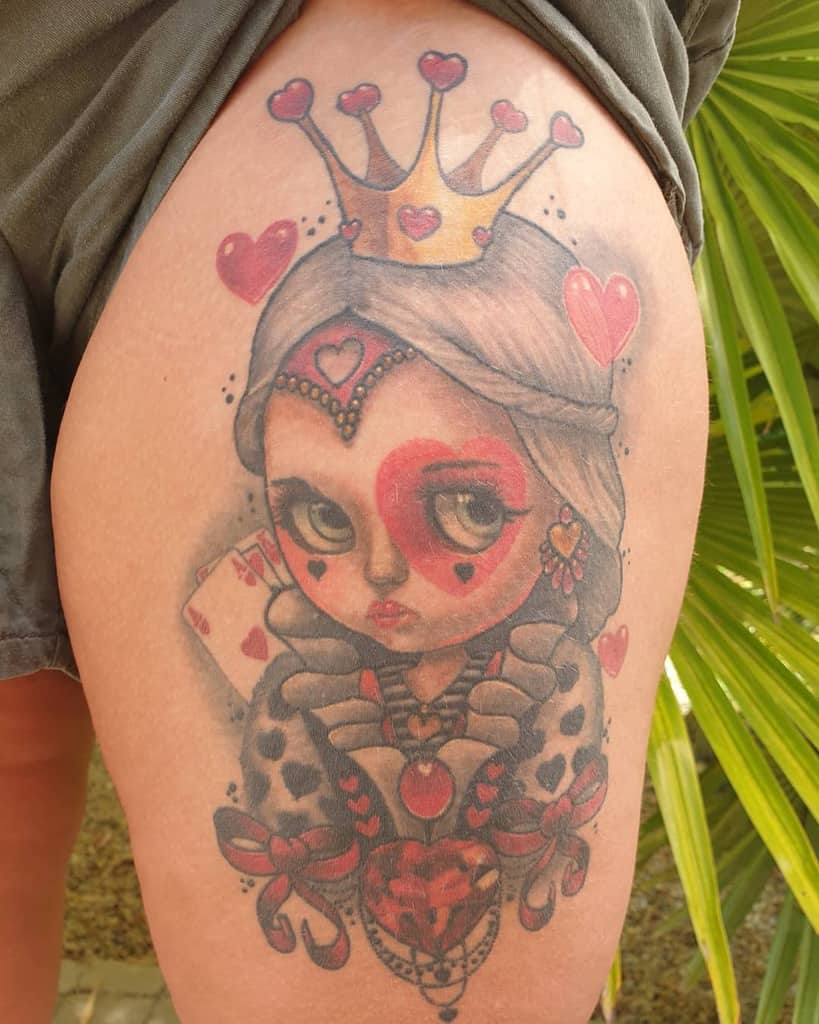 Tattoo of a queen of hearts with a crown, heart motifs, and playing card on the upper thigh