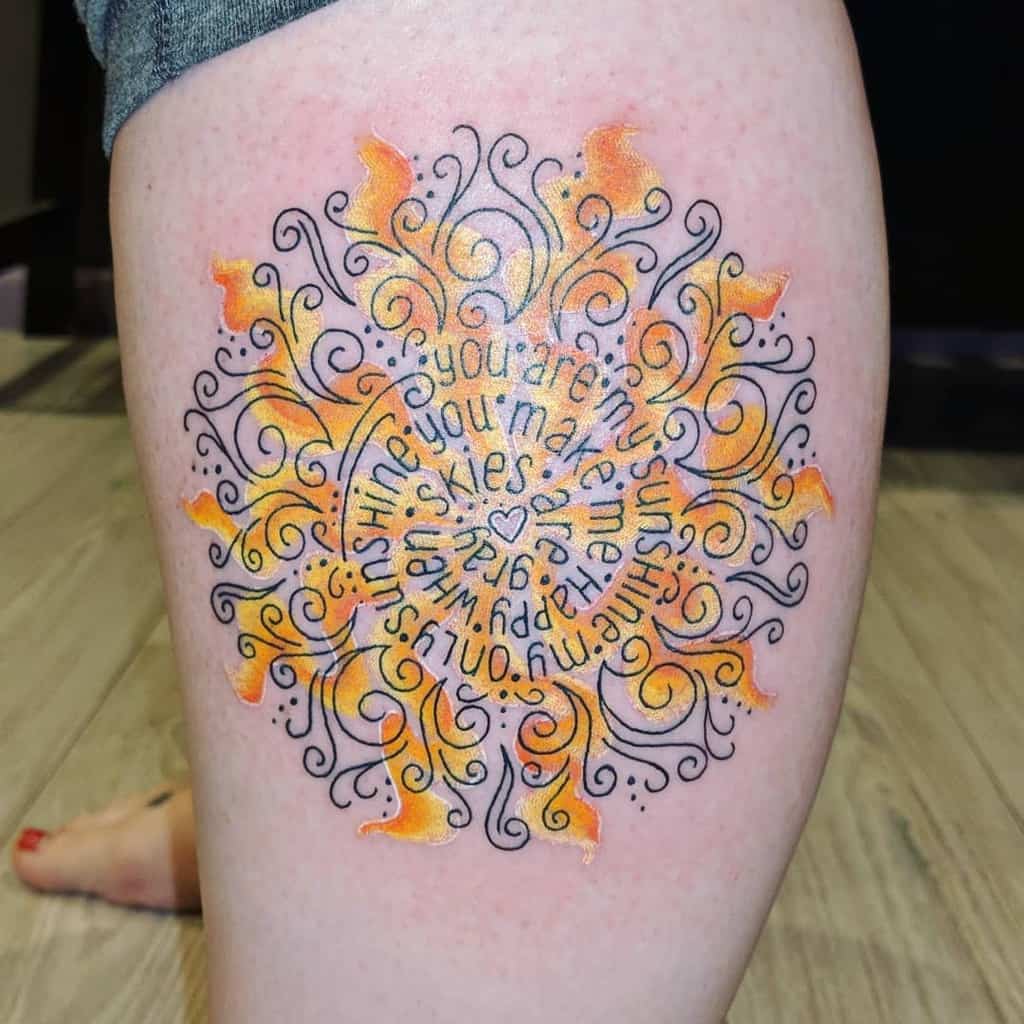 Tattoo of a yellow and black mandala with text on a thigh
