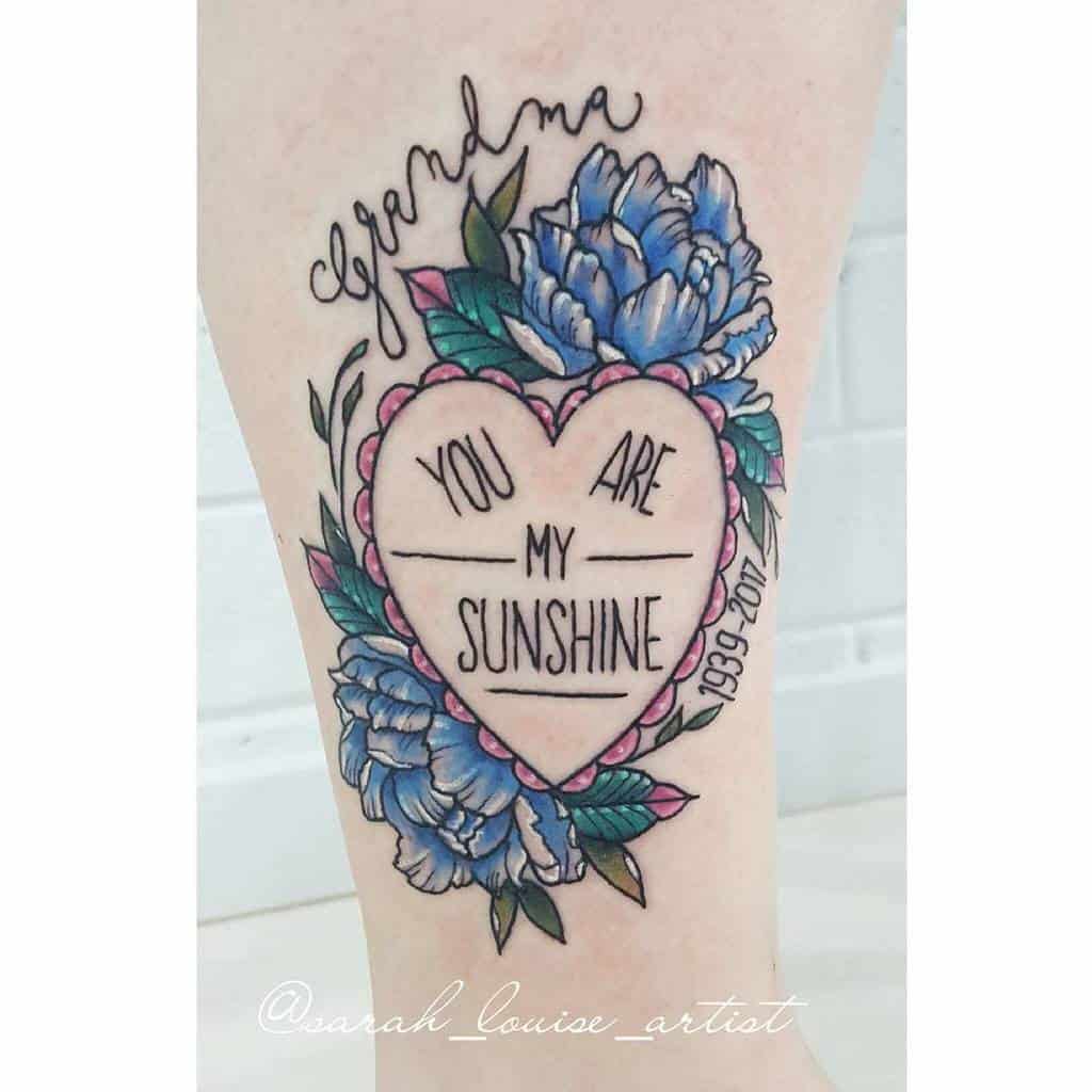 Heart-shaped tattoo with blue flowers, "Grandma, You Are My Sunshine," and dates