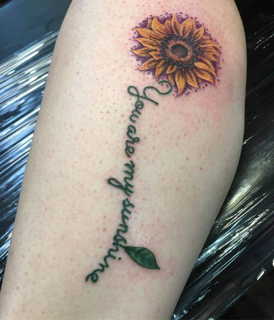 Tattoo of a sunflower with the phrase "You are my sunshine" on a leg